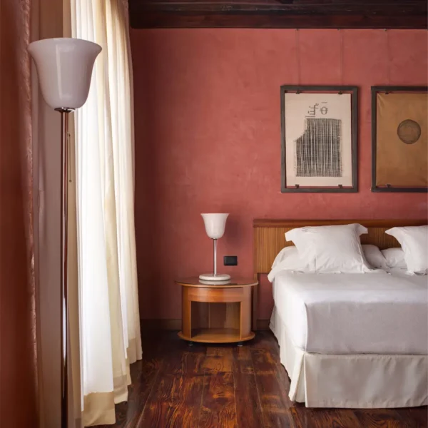 Junior suite con cama, pared en tonos rojos y arte en el Hotel San Roque